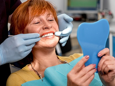 woman looking at her straight teeth in handheld mirror