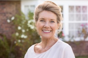 an older woman standing outside and smiling to show off her dental implants