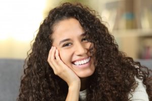 A young woman sitting indoors and smiling, showing off her healthy teeth